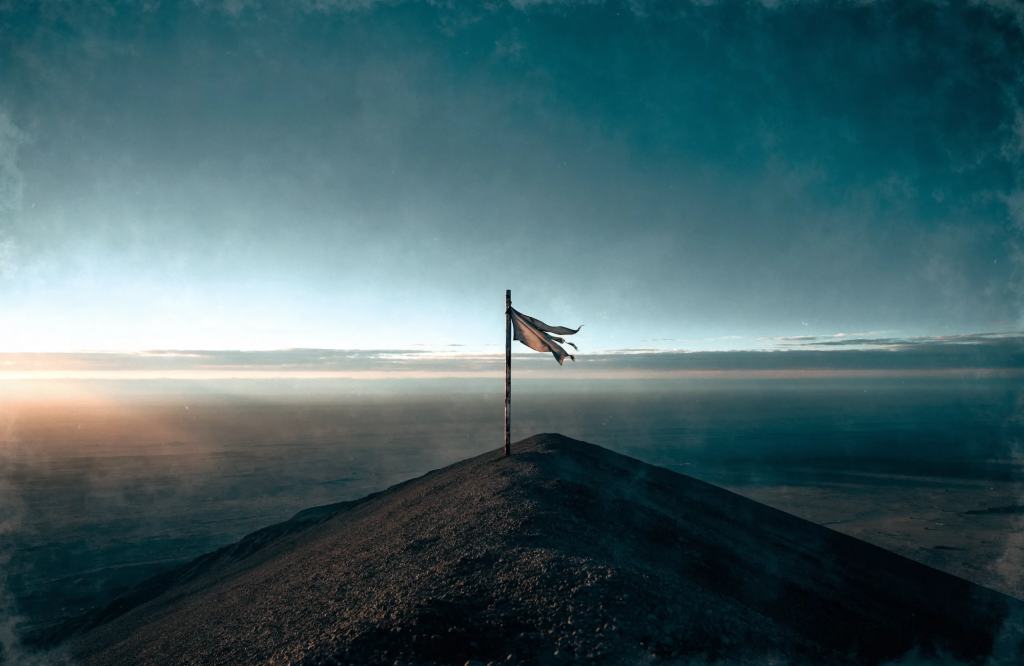 Original concept art: a single weathered marker post with a tattered flag on a bare ridge above a vast empty plain at dawn